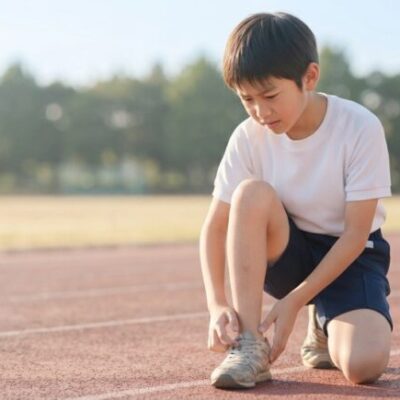 陸上のトラックで練習中にかかとの痛みを気にしてしゃがみ込む小学生の男の子のイメージ