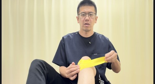 お皿の下の出っ張りの内側からお皿を包むように太ももの前の外側へテープを貼る様子