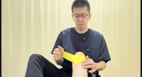 お皿の下の出っ張りの外側からお皿を包むように太ももの前の内側へテープを貼る様子
