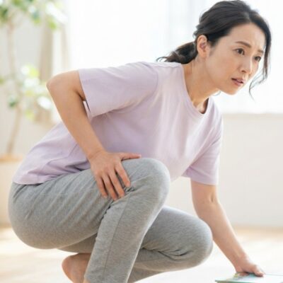 リビングでしゃがみかけて膝の裏に手を添え違和感を気にする女性のイメージ