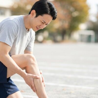 秋の運動場で走るのをやめ、片膝をついて右のふくらはぎを押さえる男性のイメージ